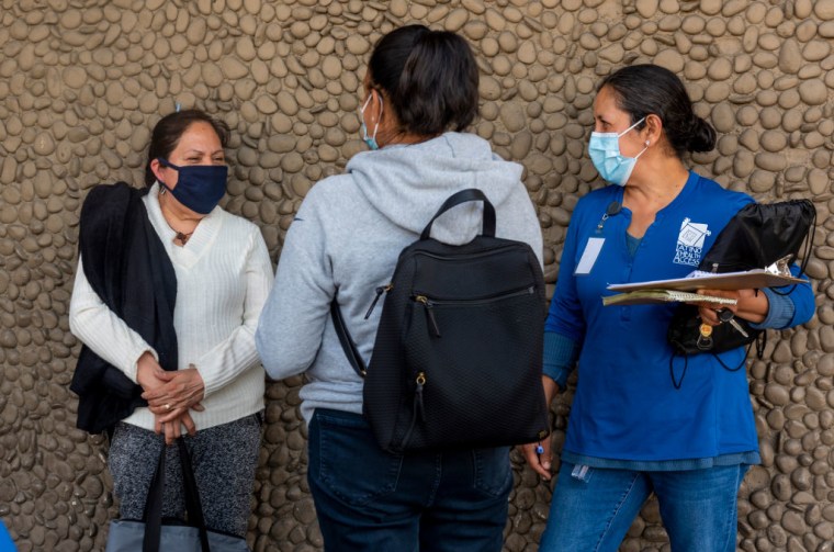 Trabajadoras de salud pública del Equipo de Respuesta de COVID de Latino Health Access, hablan con una mujer sobre cómo inscribirse para la vacuna del COVID-19 afuera de una tienda Big Saver Foods en Santa Ana el martes 27 de abril de 2021.