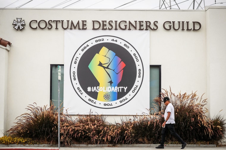 Image: A person walks by a banner hung in support of the International Alliance of Theatrical Stage Employees (IATSE) outside the Costume Designers Guild offices in Burbank, Calif., on Oct. 7, 2021.