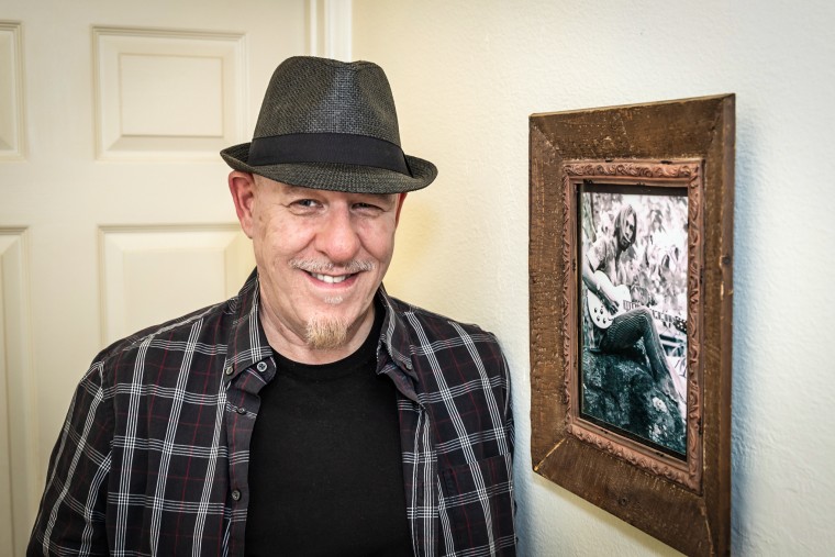 Michael Ely standing next to a photo of his spouse, James “Spider” Taylor.