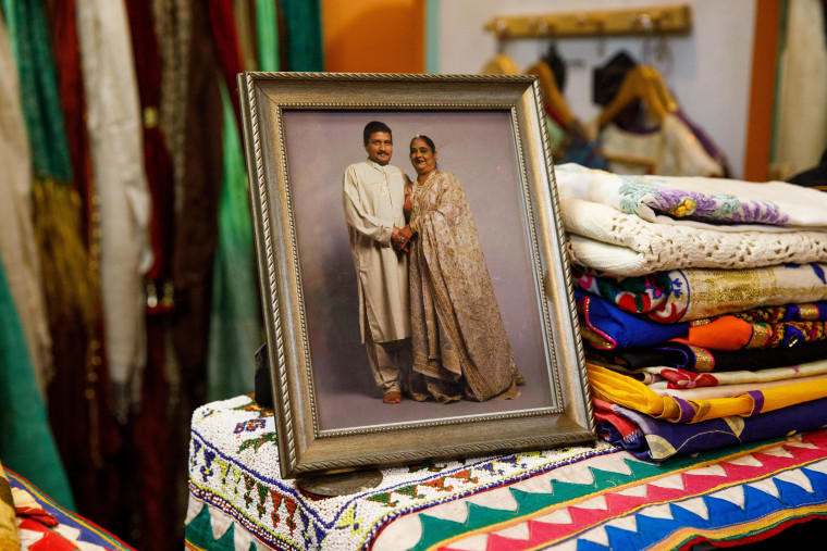 A photograph of Saroj Goyal and her husband Purushottam Goyal stands next to some fabrics inside Dress Shoppe II, the clothing boutique they opened in New York in 1977.