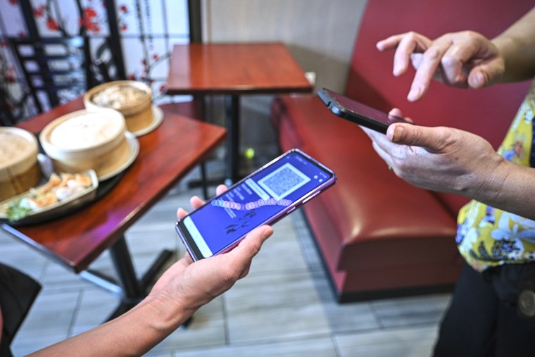 A woman holds her smartphone open to the proof of vaccination app as she waits to be seated at Shanghai Zhen Gong Fu Chinese restaurant, in Queens, N.Y., on Aug. 17, 2021.
