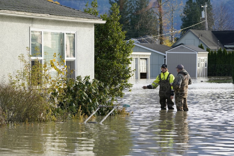 Image: Austin Holder, left, and Travis Bass stand in floodwater beside a home on Nov. 17, 2021, in Sumas, Wash.