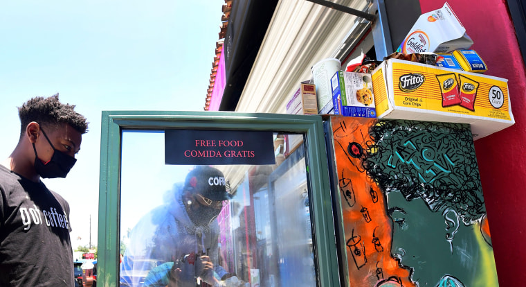 Image: Solo Morris holds the fridge door open as Danny Dierich stocks it with more items on July 16, 2020 outside the Little Amsterdam Coffee shop in Los Angeles.
