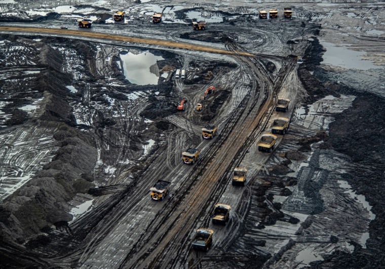 Huge trucks, some filled with oil sand and others awaiting filling, in a tar sands mine outside Fort McMurray, Alberta. From the mining operation, the sand is taken to a facility where the bitumen is separated from the sand.