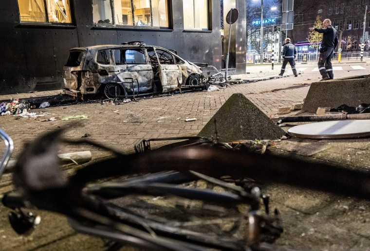 Bild: Ein Beamter zeigt auf ein verbranntes Auto, nachdem bei einem Protest gegen die teilweise Covid-Sperrung in den Niederlanden Gewalt ausgebrochen war.