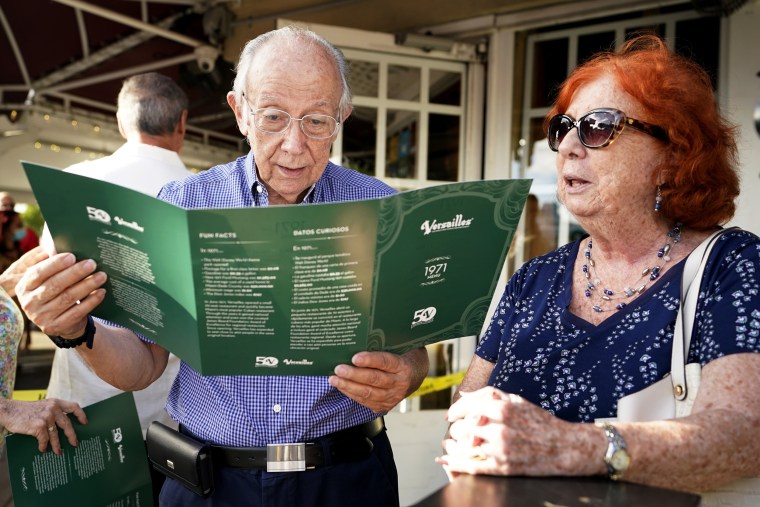 Miguel Suarez, left, reads a replica menu from 1971 before dining with his wife Yolanda at Versailles Restaurant, as the restaurant celebrates its 50th anniversary, on Nov. 10, 2021, in Miami.