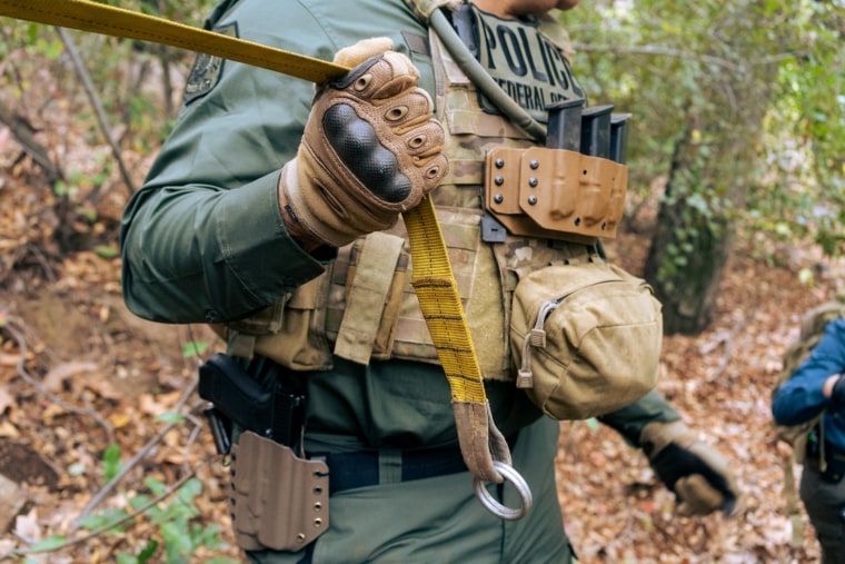 Image: A federal officer holds a rope to help the crew climb down a steep path in the forest.