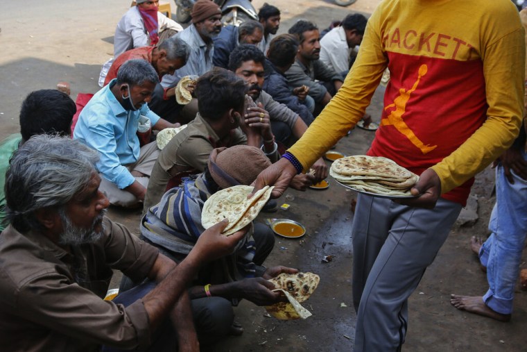 Un hombre distribuye comida a un grupo de personas sin recursos en Ahmedabad, India, el 20 de enero de 2021.