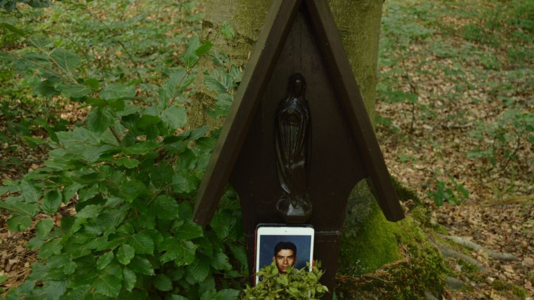 Un iPad con una fotografía de un hombre latino en uniforme, Macario García, frente a una estatua pequeña rodeada de vegetación en un bosque alemán.