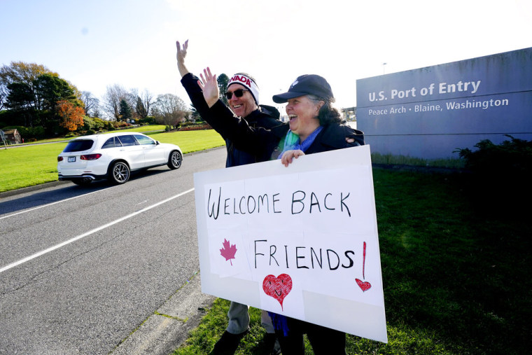 La ciudadana canadiense Traysi Spring, a la derecha, y su marido estadounidense Tom Bakken, sostienen un cartel hecho a mano para dar la bienvenida a las personas que se dirigen a Estados Unidos desde Canadá, en Blaine, Washington.