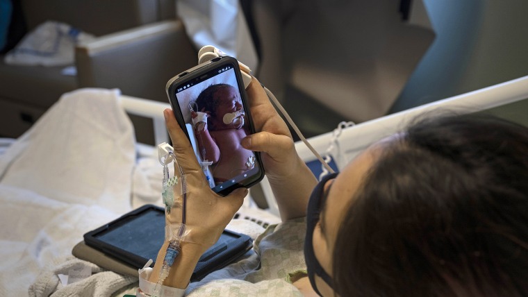 Las mujeres embarazadas que dan positivo al COVID-19 pueden tener distintas dificultades. Algunas deben ser aisladas de sus bebés luego del parto como Marisa Ponce, una joven de 18 de Texas, que mira en esta imagen a uno de sus gemelos en su teléfono en un hospital de  McAllen, en julio de 2020.