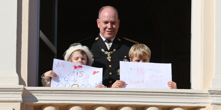 Prince Albert II of Monaco, Princess Gabriella and Prince Jacques stand with a message for Princess Charlene at the balcony of Monaco Palace during the celebrations marking Monaco's National Day on Friday.