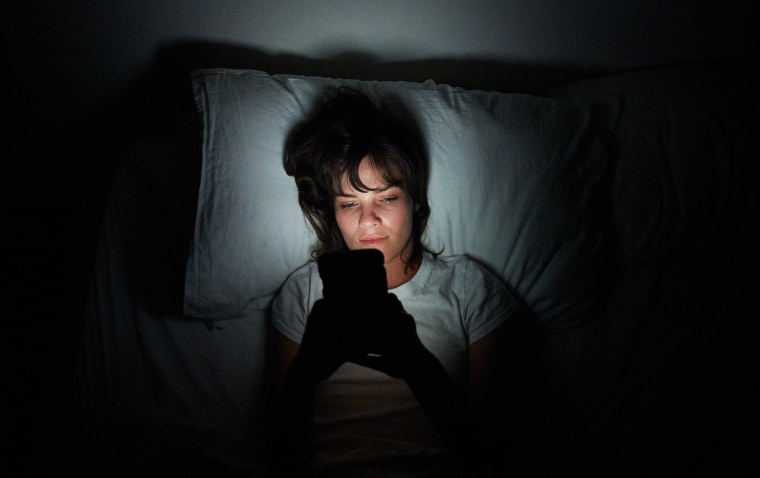 Young woman lying in bed at night using her cellphone