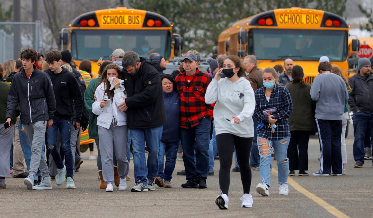Un grupo de padres se alejan junto a sus hijos de un estacionamiento, donde muchos estudiantes se reunieron tras ser evacuados del tiroteo en la escuela secundaria Oxford, en Michigan, 30 de noviembre de 2021.