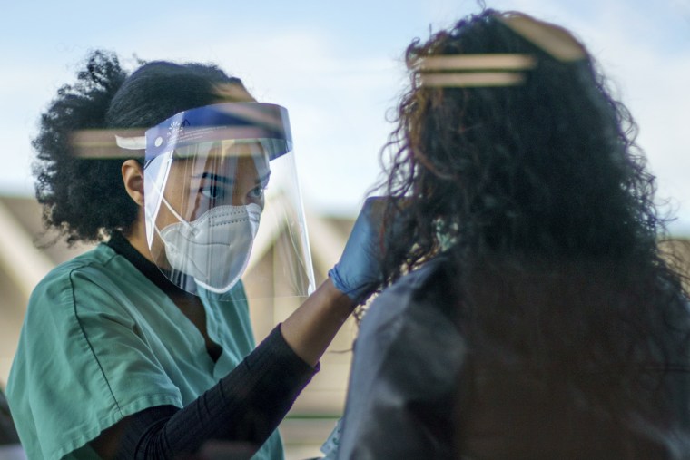 woman in scrubs wearing mask and face shield tests patient for COVID-19.