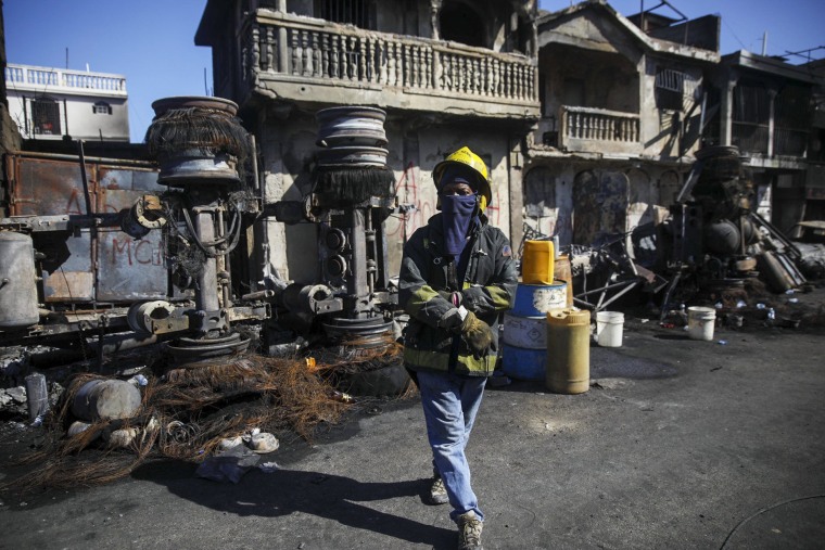 A firefighter stands next to the remains of a truck that was carrying gasoline and overturned in Cap-Hatien, Haiti, on Dec. 14, 2021. The truck exploded, engulfing cars and homes in flames, killing more than 50 people and injuring dozens of others.