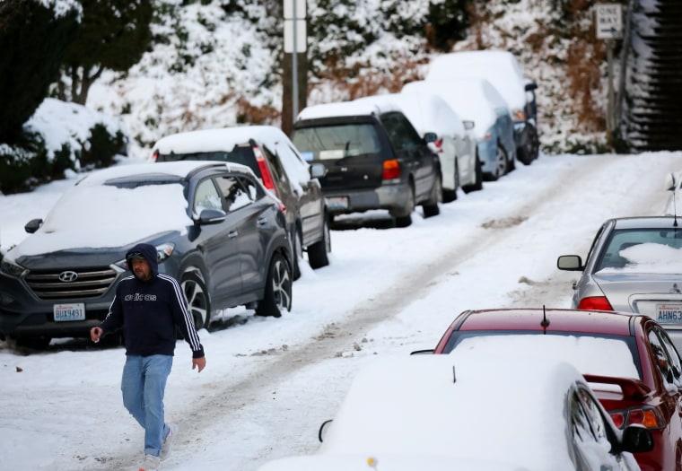 A man walks by cars on an incline with several inches of snow accumulated after a recent snowfall in Seattle, Washington, on Dec. 27, 2021.