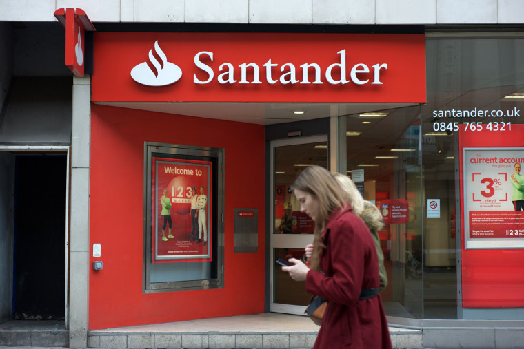 Image: People walk past a Santander bank branch in Manchester, England.