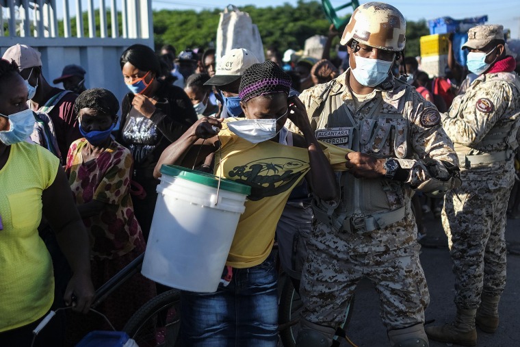 Una mujer, a quien se le niega la entrada a la República Dominicana, intenta ponerse su mascarilla protectora mientras un soldado la saca de una fila en el cruce fronterizo en Dajabón, República Dominicana, el viernes 19 de noviembre de 2021.