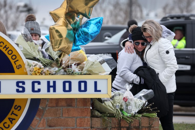 Dos mujeres se abrazan frente a un pequeño altar improvisado junto a la Escuela Secundaria de Oxford, Michigan, en homenaje a las víctimas del tiroteo, el 1 de diciembre de 2021.