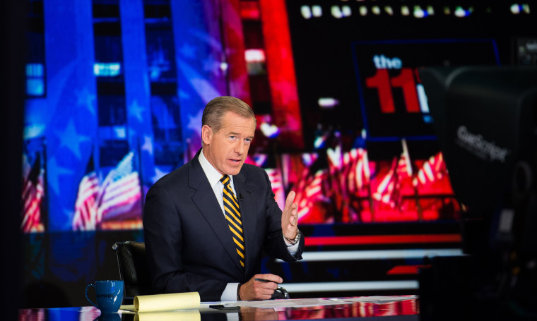 Brian Williams gestures at the camera while reporting behind an anchor desk with a red and blue background.