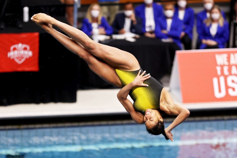 A Black woman in a yellow and black bathing suit grimaces as she twists headfirst into the water.