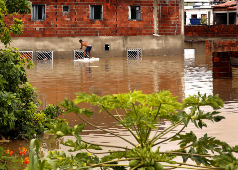 Un hombre intenta recuperar muebles por la ventana de una casa debido a las inundaciones provocadas por las intensas lluvias en la ciudad de Itapetinga, en la región sur del estado de Bahía, Brasil, el domingo 26 de diciembre de 2021.