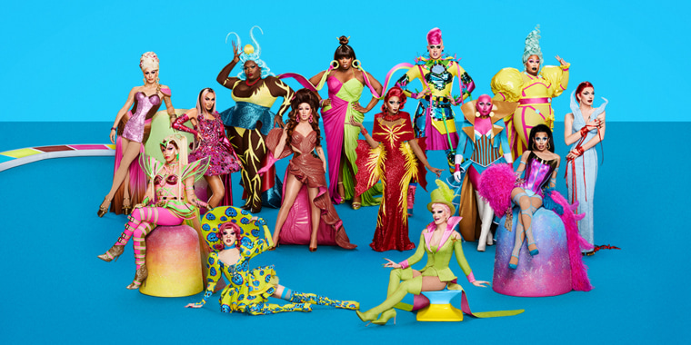 The queens stand in bright costumes in front of a blue background