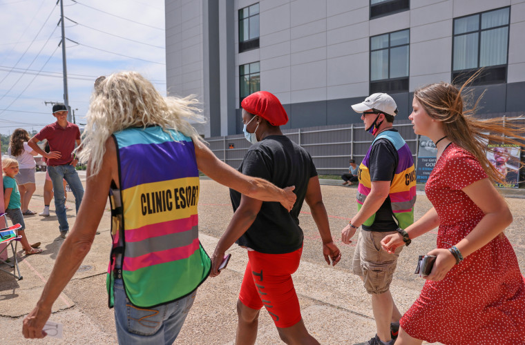 A clinic escort leads a woman surrounded by anti-abortion protesters at the Jackson Women's Health Organization in Jackson, Miss.