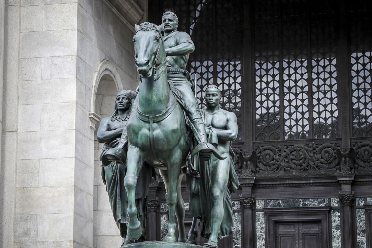 A bronze statue of Theodore Roosevelt on a horse with a Native American man on one side and an African man on the other side stands in front of the American Museum of Natural History on June 30, 2020 in New York.