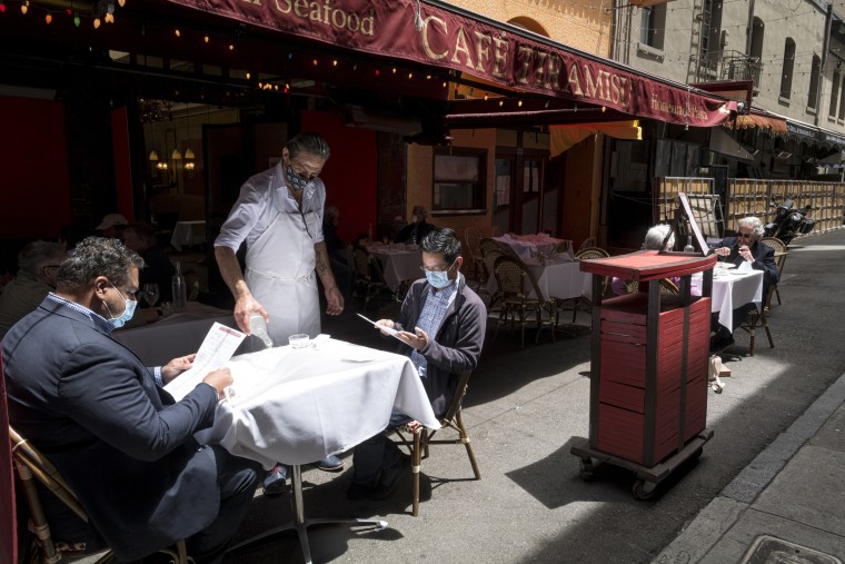 Image: Guests wear protective masks as a waiter serves drinks at a restaurant in San Francisco on June 15, 2020.