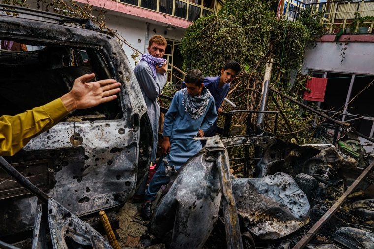 Image: Relatives and neighbors of the Ahmadi family gather around the incinerated husk of a vehicle targeted and hit by an U.S. drone strike that was supposed to target ISIS-K suicide bombers but instead killed civilians in Kabul, Afghanistan on Aug. 30, 2021.