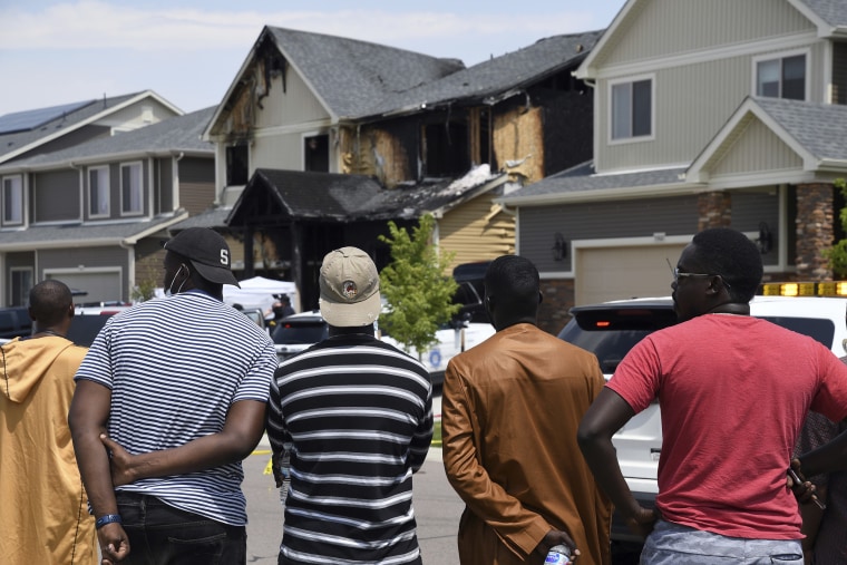 A group looks on at the house where five people, including a 22-month-old child, were found dead after a fire, in suburban Denver on Aug. 5, 2020.