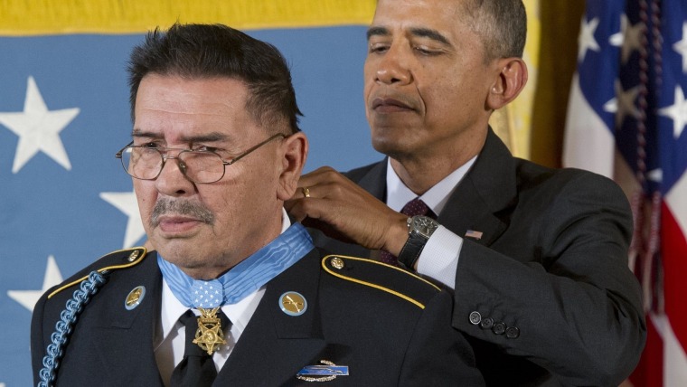 El expresidente Barack Obama pone una medalla alrededor del cuello del veterano Santiago Erevia, latino con lentes y bigote.