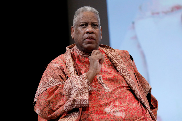 Andre Leon Talley looks thoughtful in a reddish orange caftan of sorts with short white and gray hair