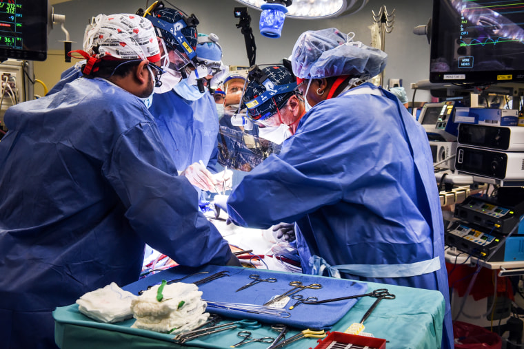 Doctors in blue scrubs huddle around an operating table