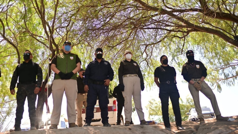 Seis agentes del orden público dedicados a controles migratorios, con cubrebocas y uniforme de pantalones khaki y camiseta negra, posan cerca de la frontera de México con Estados Unidos.
