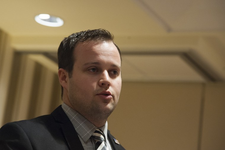A close up photo of Josh Duggar  in a suit and tie in a generic beige conference room.