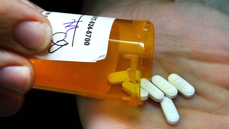 Una persona inclina una botella naranja de analgésicos opioides y seis pastillas largas de color blanco caen sobre su mano