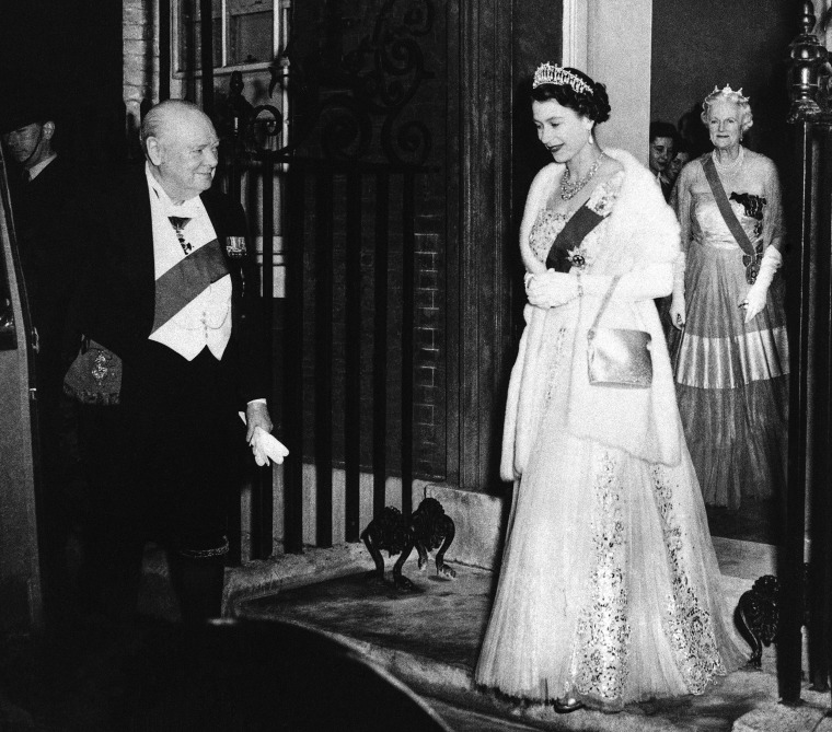 British Prime Minister Winston Churchill bids farewell to Queen Elizabeth II at the end of a dinner he hosted at No. 10 Downing Street in London on April 4, 1955. Lady Churchill stands in the doorway as she follows the queen.