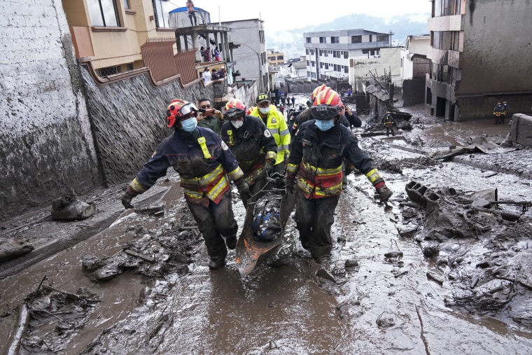 Rescue workers carry away the body of a victim after flash flooding triggered by rain filled up nearby streams that burst their containment mechanisms, collapsing a hillside and bringing waves of mud over homes in the La Gasca area of Quito, Ecuador, on Feb. 1, 2022.