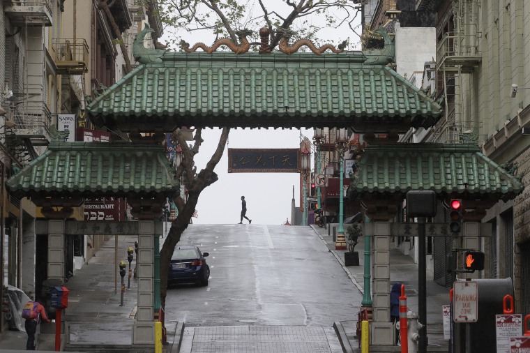 A pedestrian crosses Grant Street behind the Dragon Gate, an entrance to Chinatown in San Francisco on April 4, 2020.