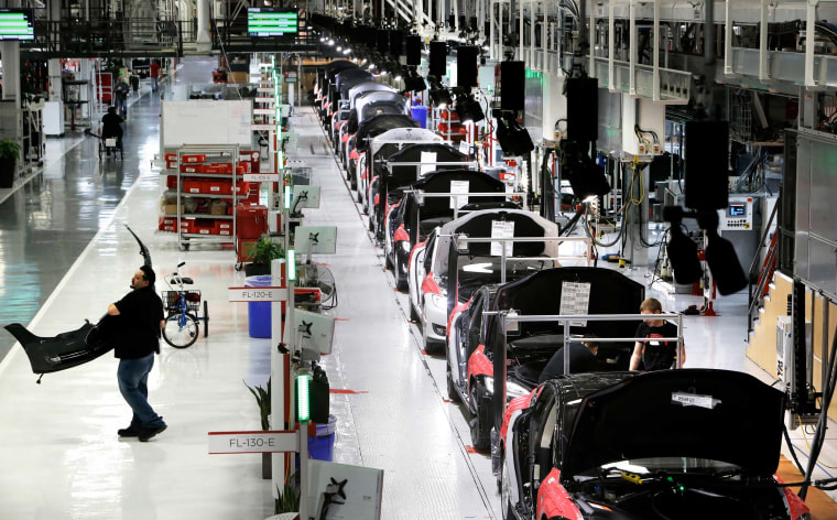 A worker carries a front end part along the assembly at Tesla Motors on February 19, 2015 in Fremont, CA.