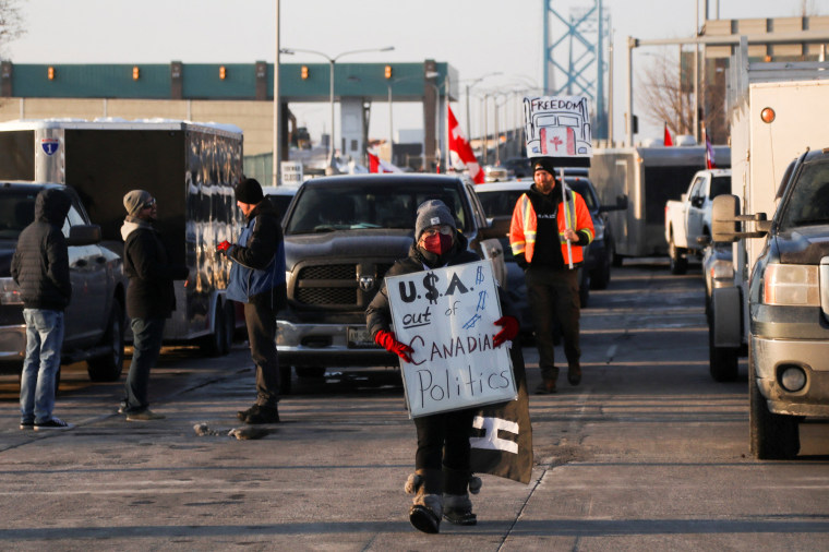 Image: A protester holds a sign that reads, " USA Out of Canadian Politics" as vehicles block the route leading from the Ambassador Bridge, linking Detroit and Windsor, during a protest against vaccine mandates, in Windsor, Ontario, Canada on Feb. 8, 2022.