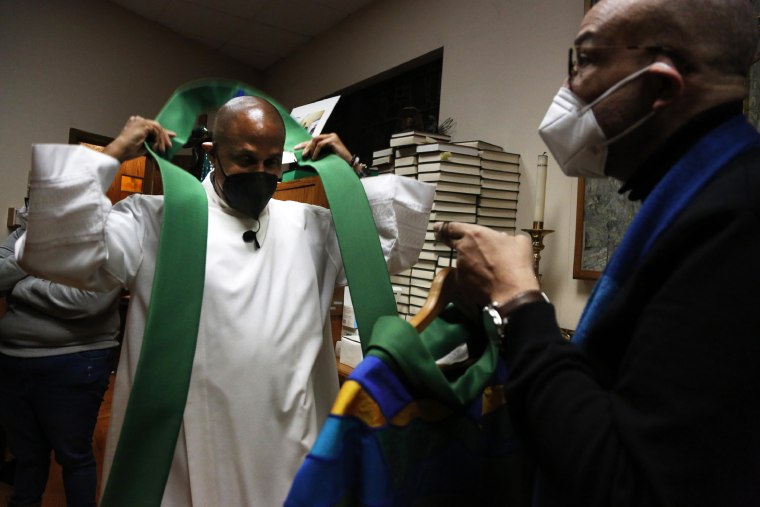 The Rev. Bryan Massingale, left, prepares for Mass with the help of sacristan Darren Johnson, right, on Jan. 30, 2022, at St. Charles Borromeo Catholic Church in the Harlem neighborhood of New York.