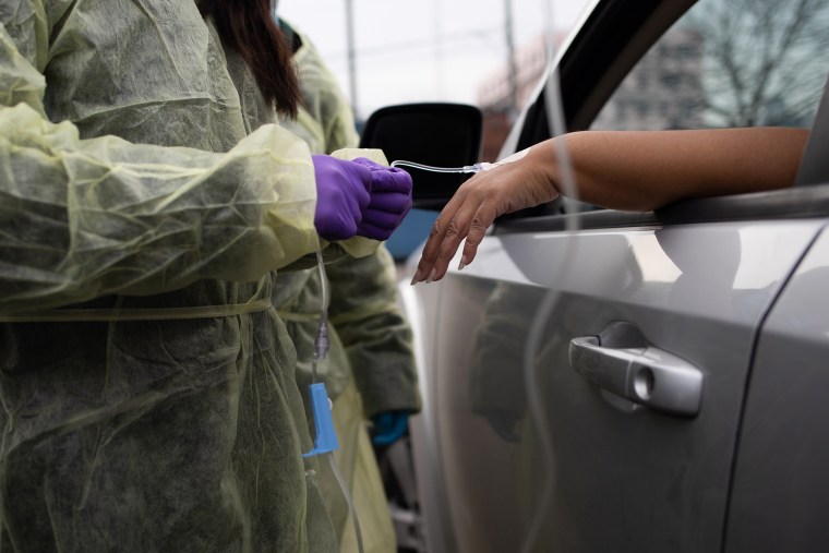 Image: A healthcare worker attaches an IV infusion to a patient's hand during a monoclonal antibody treatment in the parking lot at Wayne Health Detroit Mack Health Center in Detroit on Dec. 23, 2021.