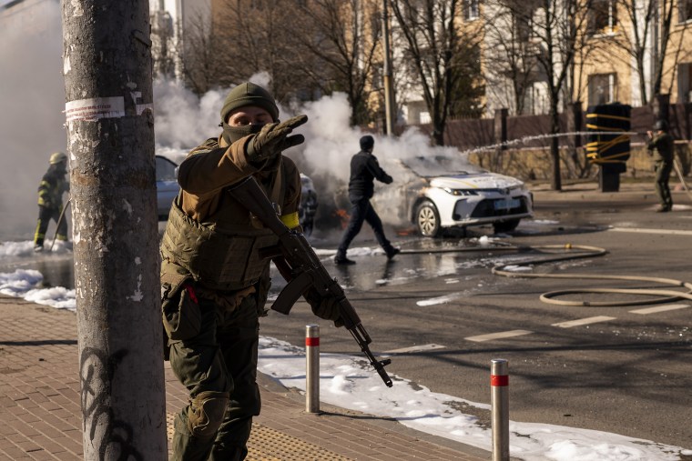 Ukrainian soldiers take positions outside a military facility in Kyiv on Saturday as two cars burn in the street.