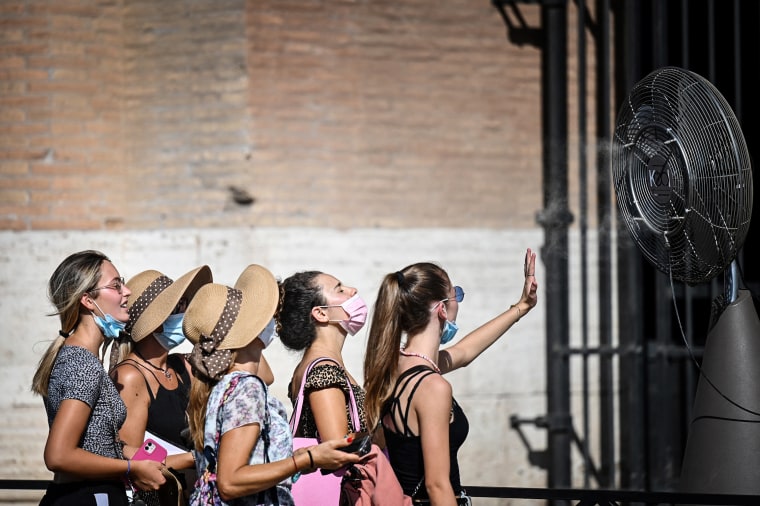 A group of woman cool off in front of a cooling fan during a heatwave as they queue at the entrance of the Colosseum in Rome on Aug. 12, 2021.