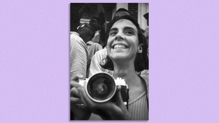 Una mujer latina sonríe mientras sostiene una cámara análoga