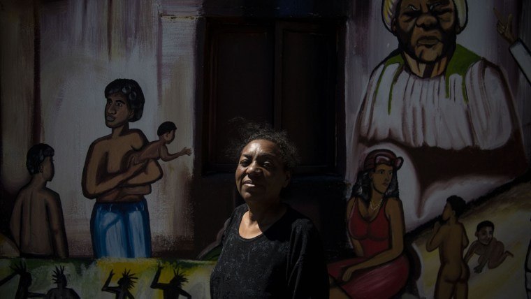 Una mujer mexicana negra mira a la cámara frente a una serie de murales que muestran a personas afrodescendientes.